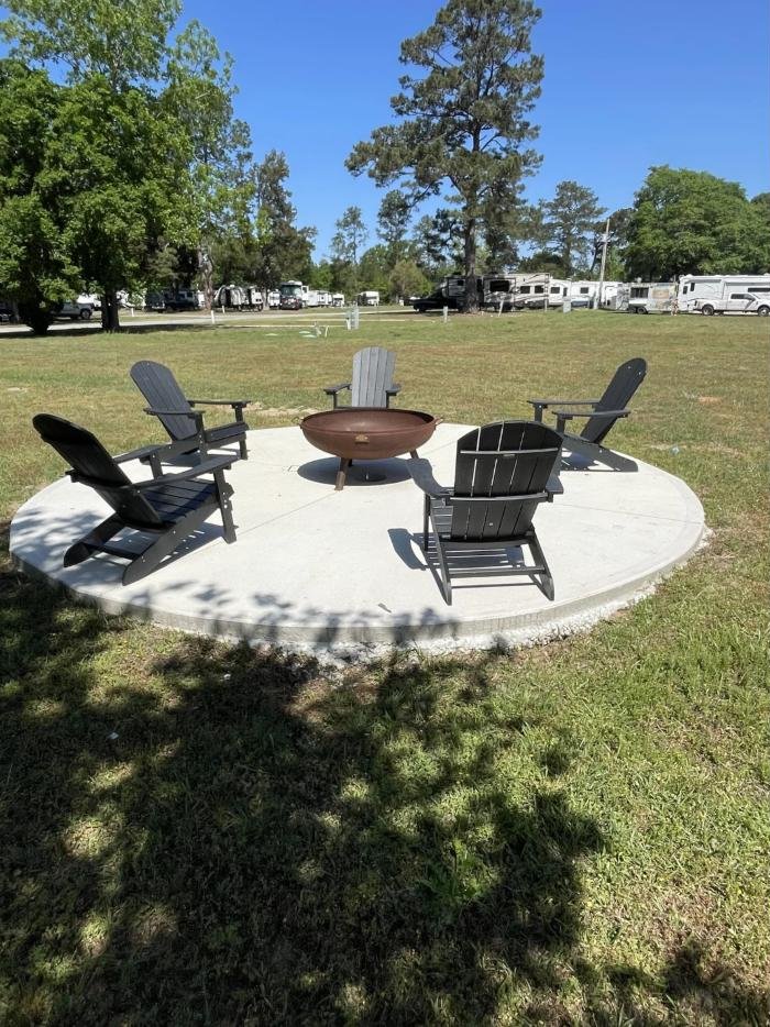 Fire pit ringed with Adirondack chairs, with RVs parked beyond
