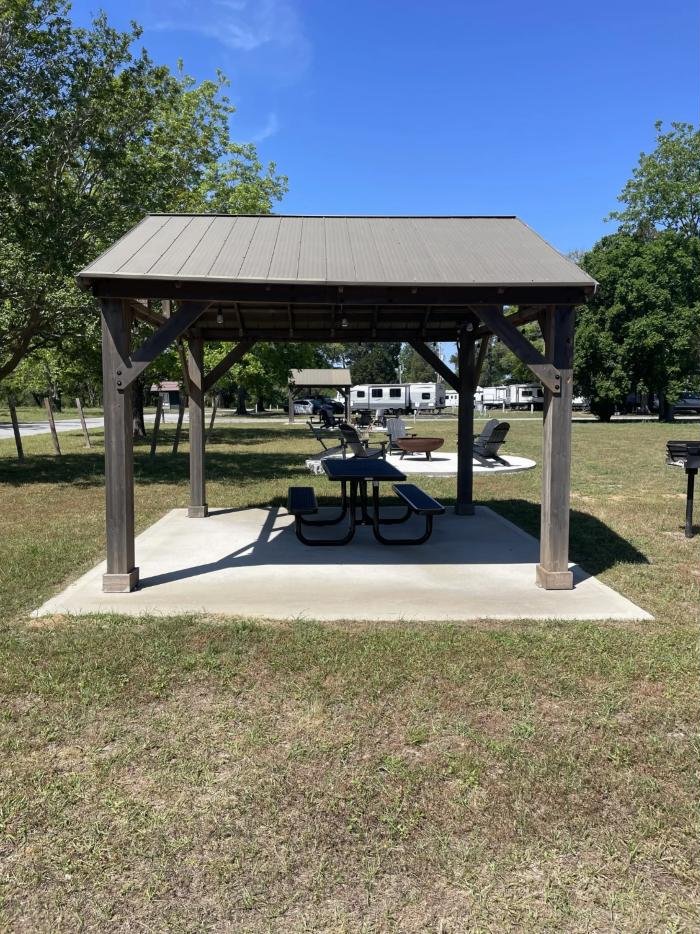 Covered wooden picnic pavilion with a picnic table and charcoal grill